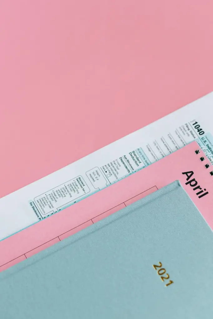 A close-up of tax forms with an April calendar on a pink surface, representing tax season.