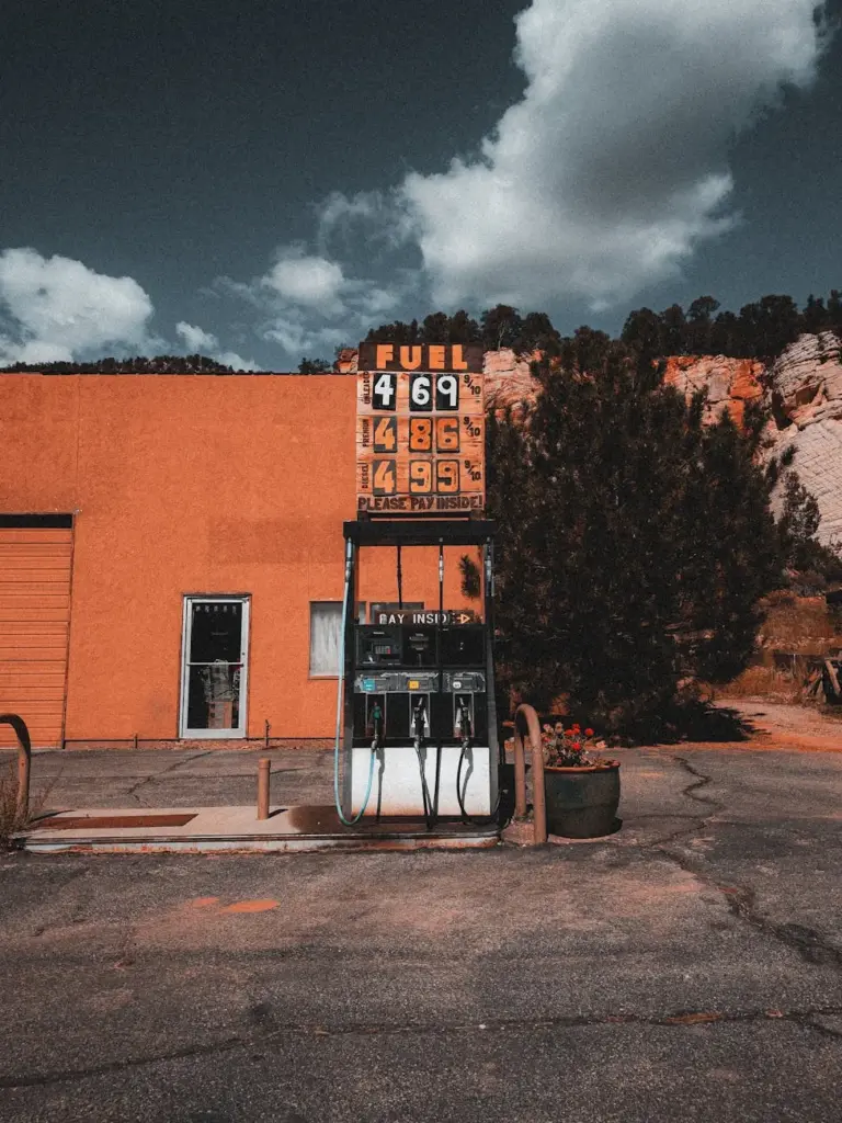 Old gas station with vintage pump and price sign under a cloudy sky. Outdoors setting.