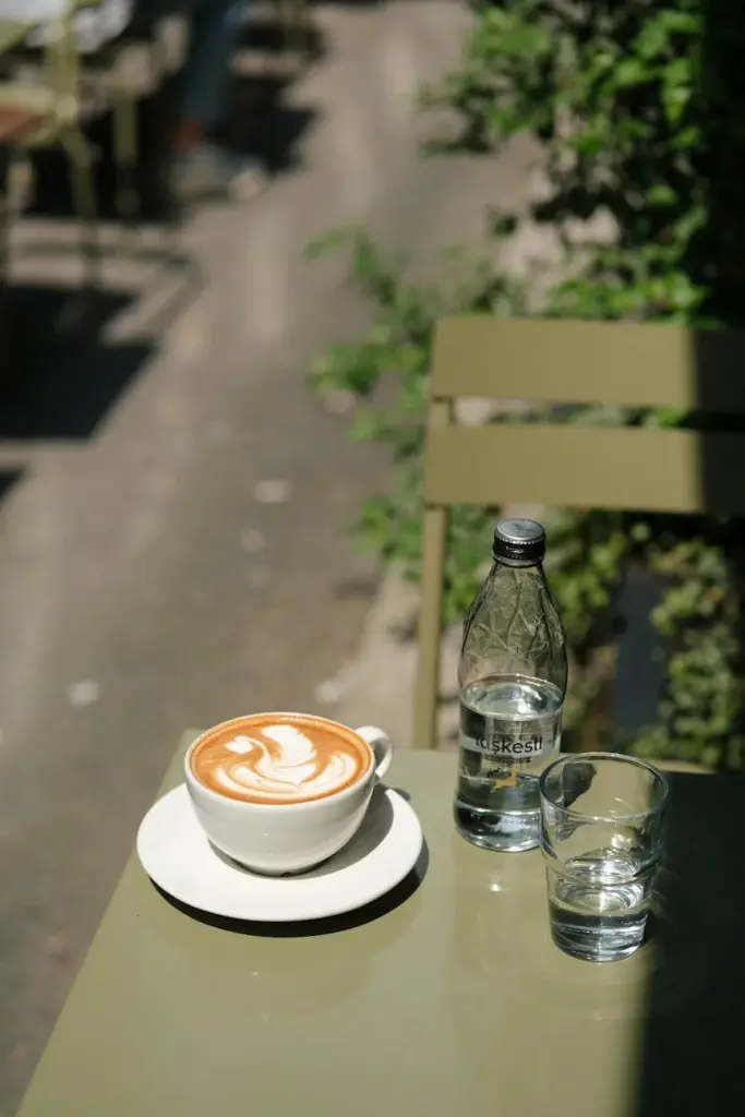 Outdoor cafe setting with latte art and bottled water on a sunny day.