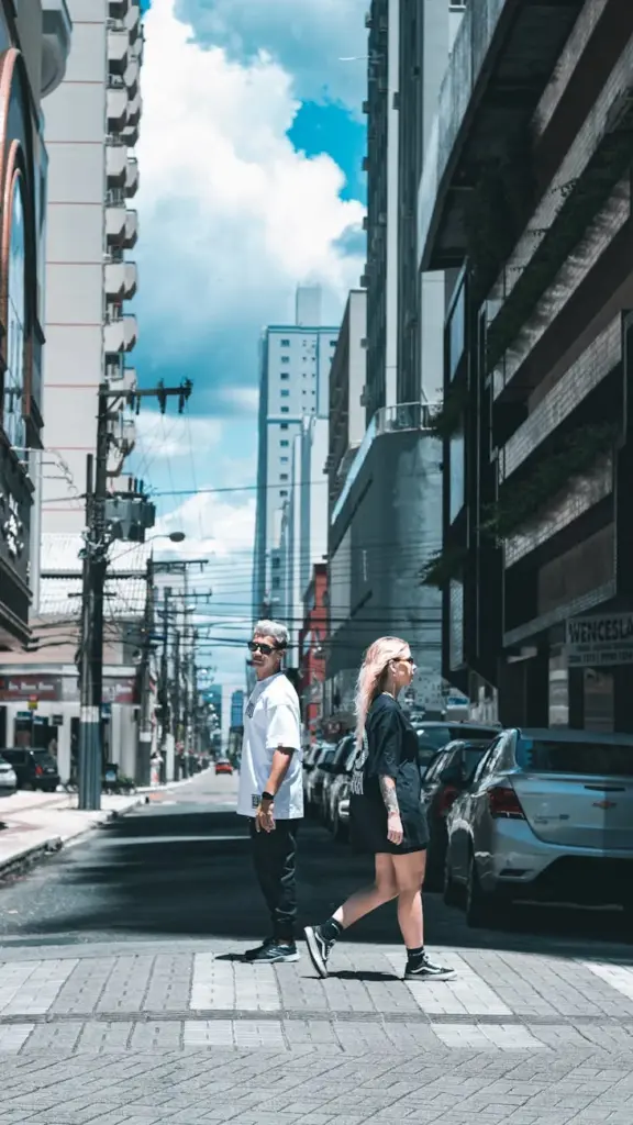 Two adults crossing a busy city street against a backdrop of towering buildings and blue sky.