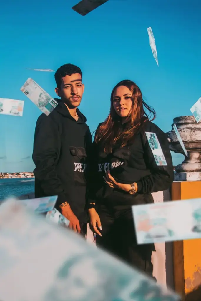 Young man and woman in black clothes on quay in sunny day looking at camera while banknotes flying around