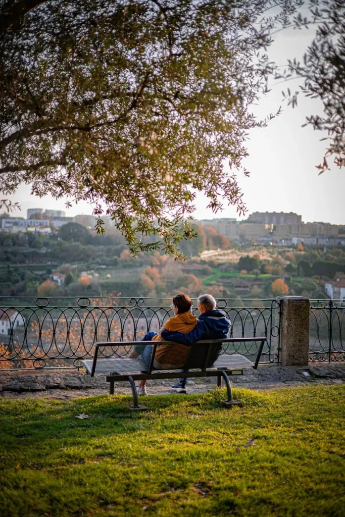 A couple enjoys serene park views on a wooden bench in Porto, Portugal.