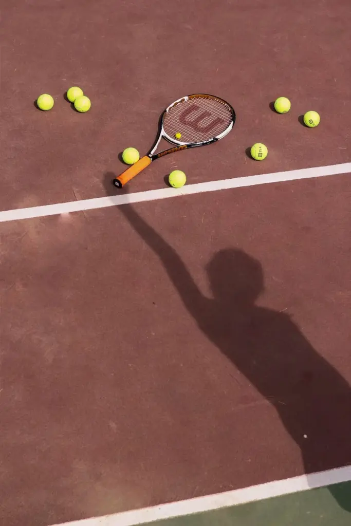 Shadow of player reaching out to tennis racket and balls on a court.