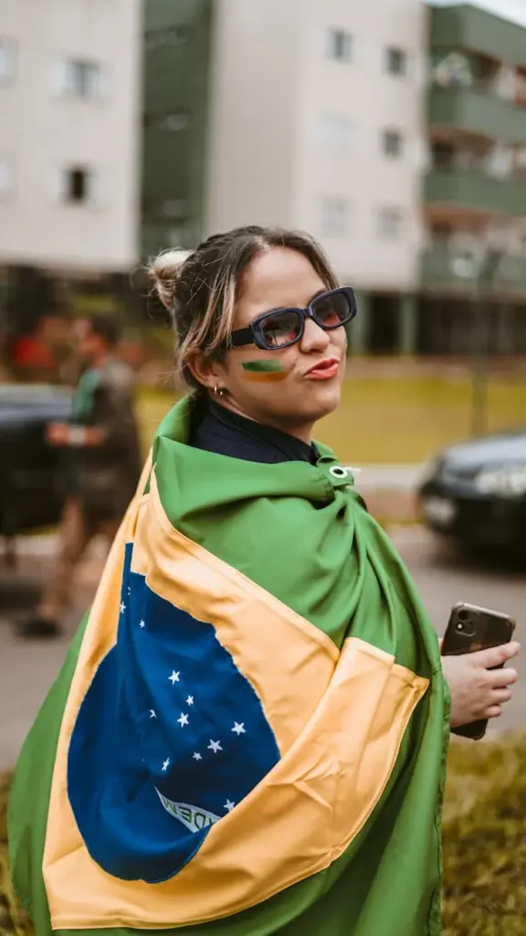 Woman wrapped in Brazilian flag standing outdoors with painted face.