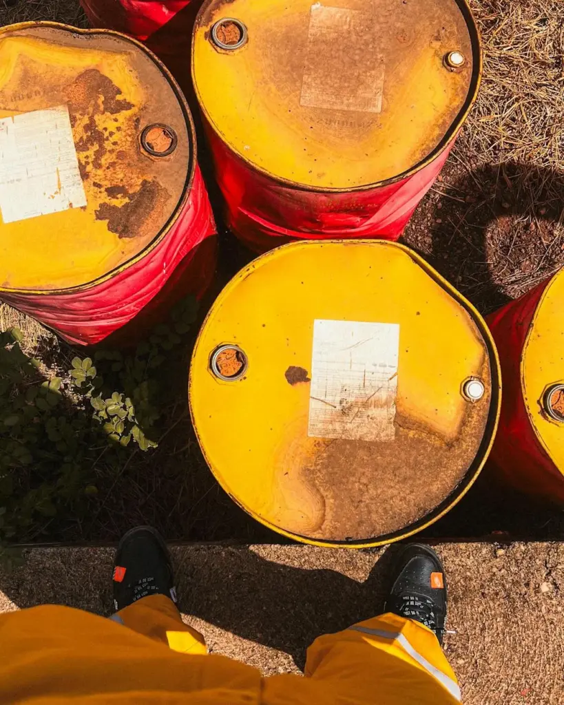 Top view of weathered yellow oil barrels on ground, person visible wearing yellow pants.