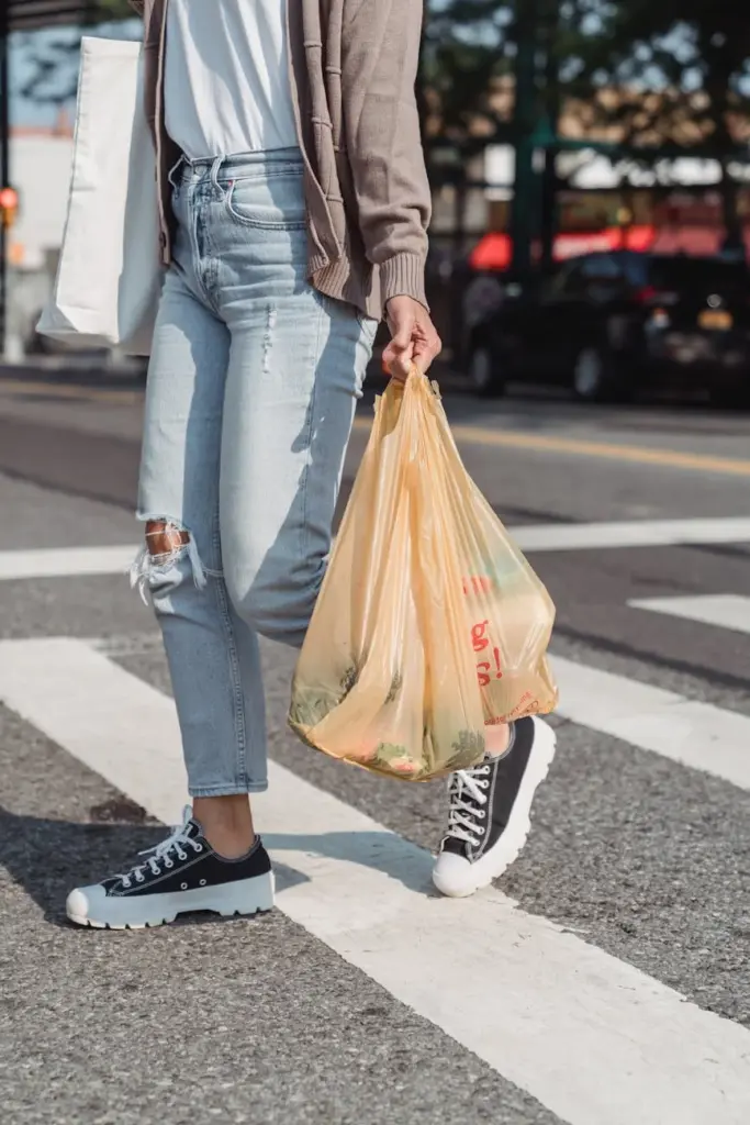 Casual street scene of a person carrying grocery bags while crossing at a pedestrian lane.
