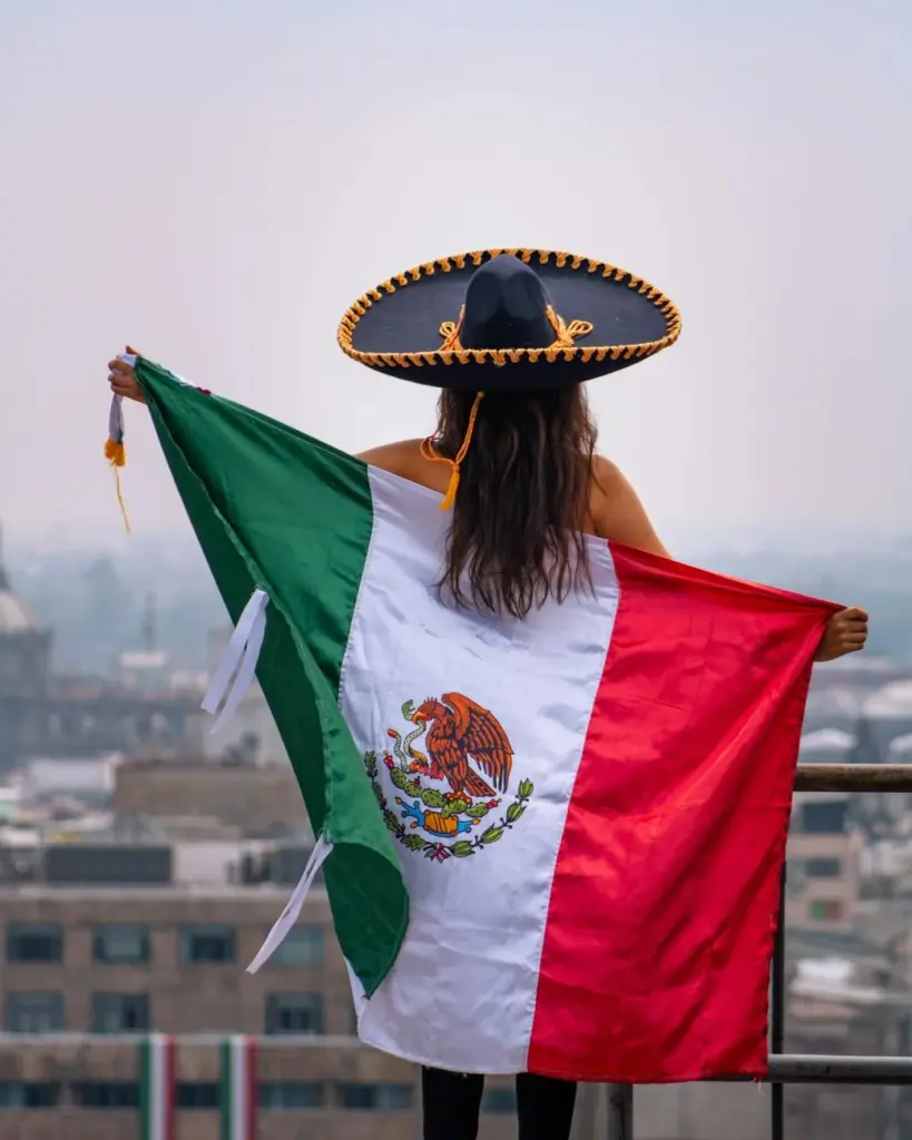 A woman in a sombrero holds the Mexican flag overlooking Mexico City, capturing cultural essence.