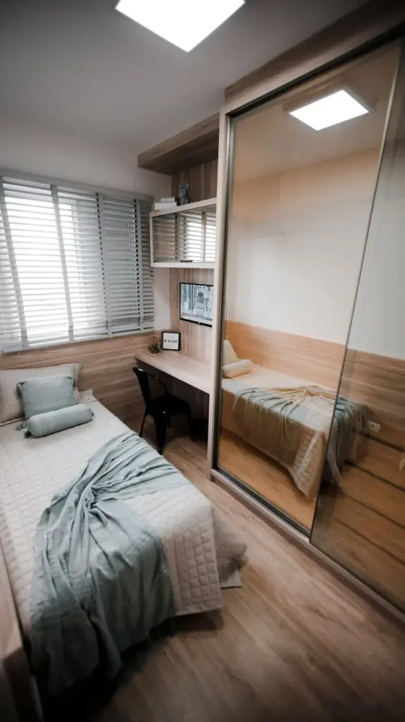 A small modern bedroom with minimalist decor and a large mirror reflecting the space.