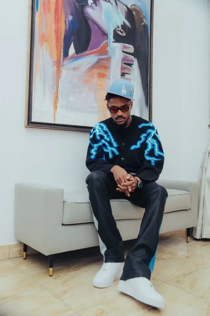Man in vibrant streetwear outfits sitting on a couch under abstract art.