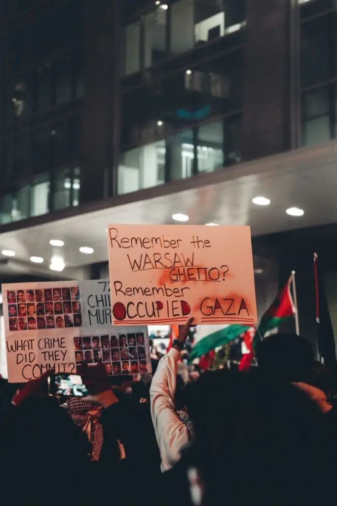 Crowds hold protest signs at night in an urban setting. Demonstration highlights social issues.