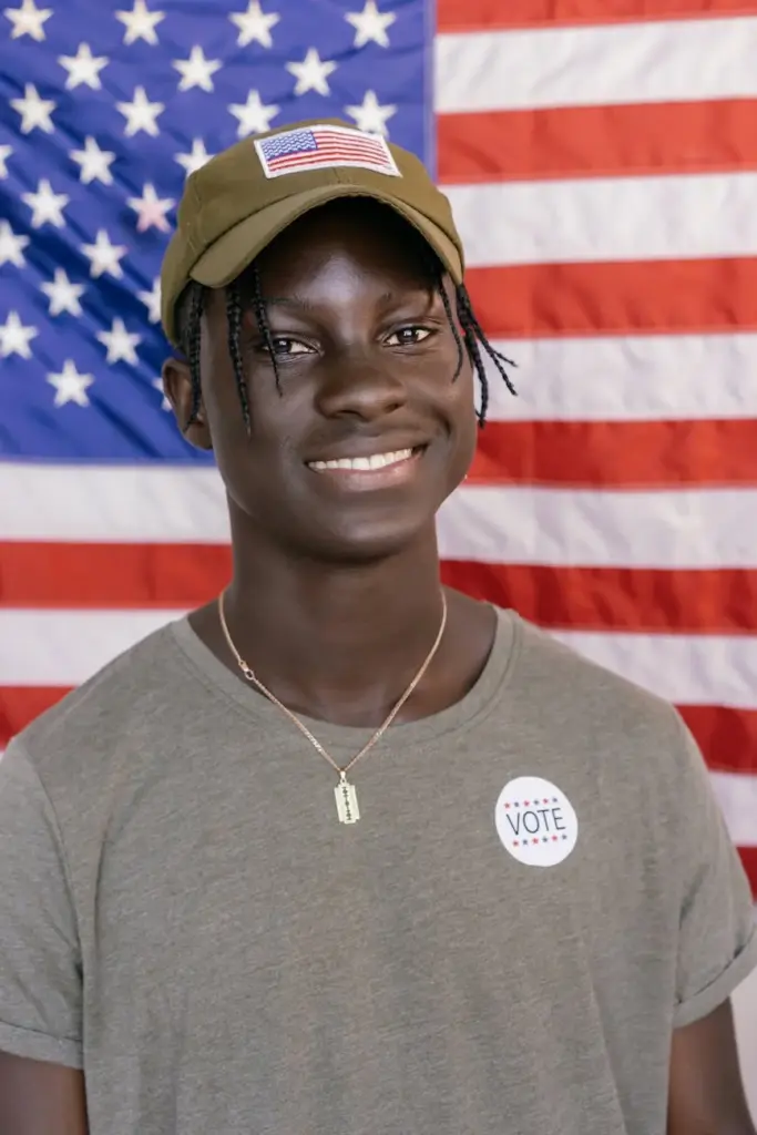 Smiling young voter in front of American flag wearing a "Vote" sticker.