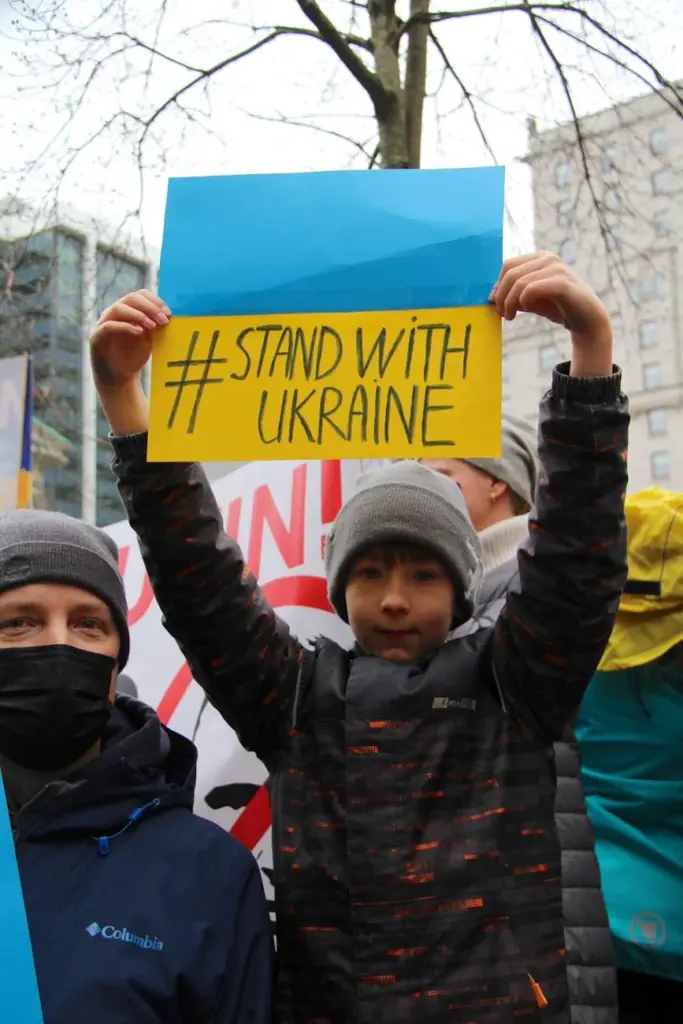 A boy holds a '#StandWithUkraine' sign at a supportive rally in Vancouver, Canada.