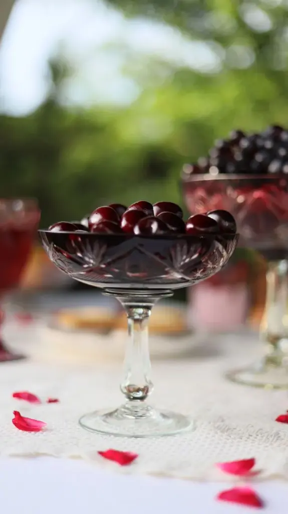 A delicate crystal bowl filled with ripe cherries on an outdoor table setting.