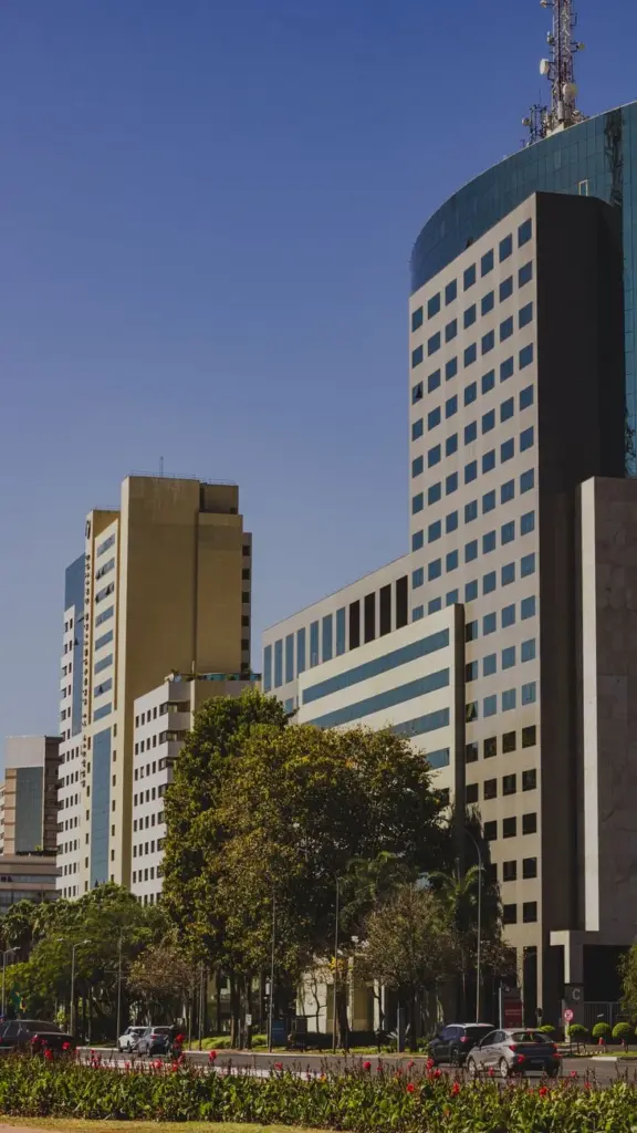 A view of modern office skyscrapers in Brasília with trees and cars in foreground.