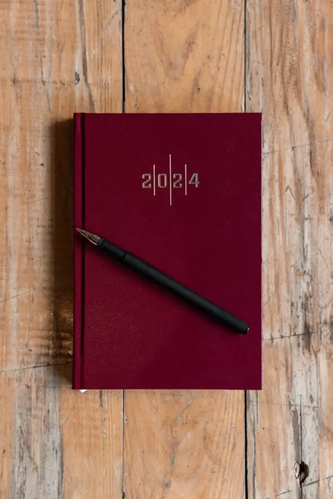 Stylish burgundy 2024 planner with a pen, perfect for organizing and planning.