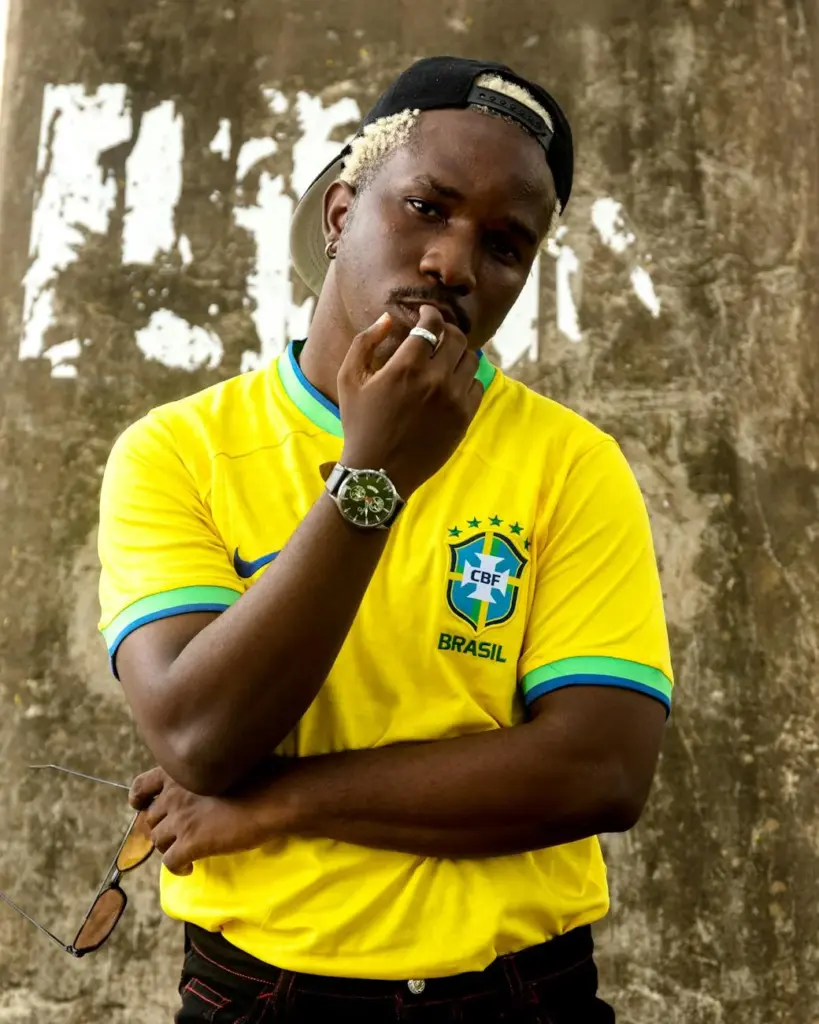 Young man in Brazil soccer jersey posing against a gritty wall background.