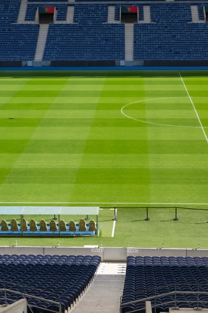 A vertical view of an empty soccer stadium in Porto, Portugal. Sunlight casts shadows on the green field.