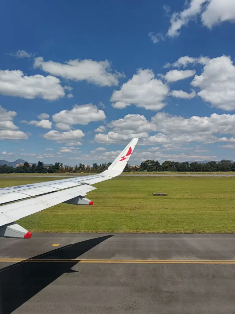 Airplane wing on the runway with blue skies and scattered clouds, ready for takeoff.