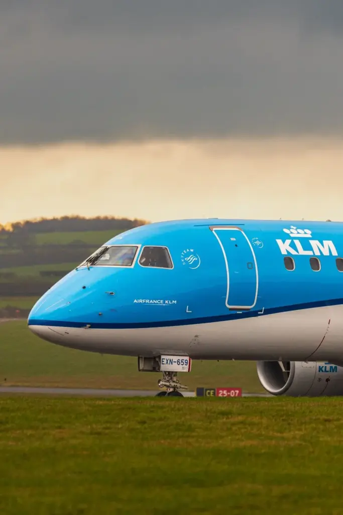 A KLM airplane on the runway against a dramatic sky and green landscape.