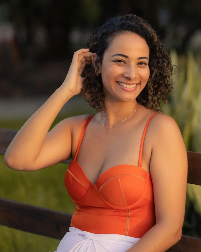A cheerful woman in an orange dress smiles warmly during a sunset outdoor portrait session.