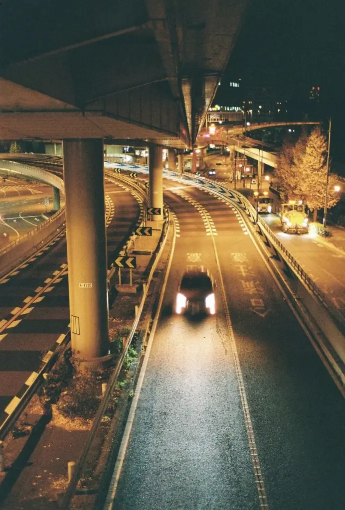 A single car drives on a deserted highway under streetlights at night.