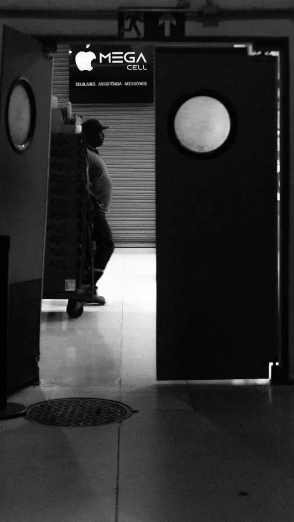 Black and white image of a worker standing behind a partially open warehouse door.