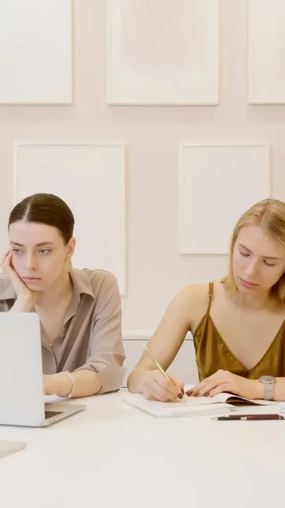 Two women working together at a desk in a modern office setting.