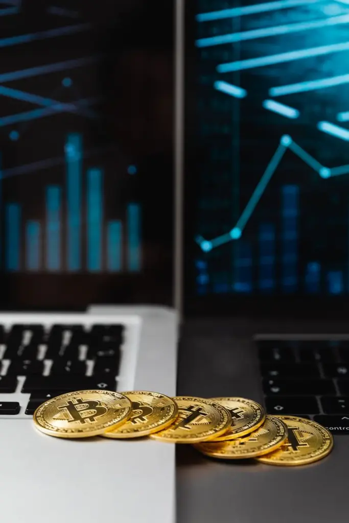Close-up of golden bitcoins between laptops displaying trading graphs, symbolizing cryptocurrency and blockchain technology.