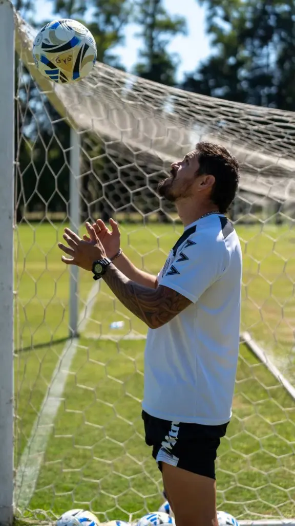 Male soccer player practicing heading skills near a goalpost on a sunny day.