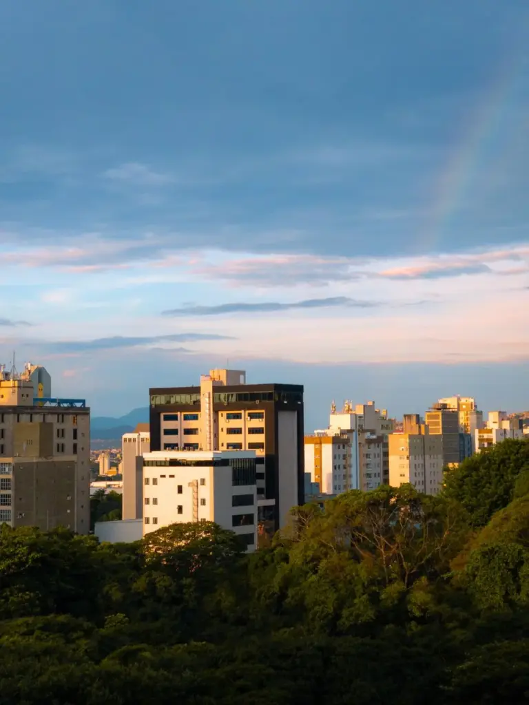 Cityscape of Belo Horizonte at dusk with a rainbow above the skyline.