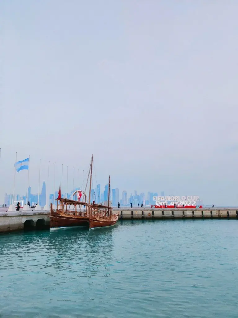 Traditional Dhow boat docked at Doha Harbor with FIFA World Cup sign, scenic city skyline in the background.