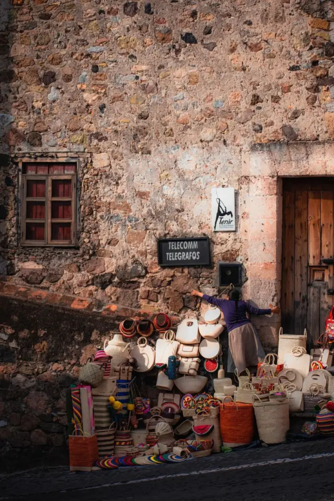 Colorful handmade baskets displayed outside a rustic stone building in Taxco, Mexico.