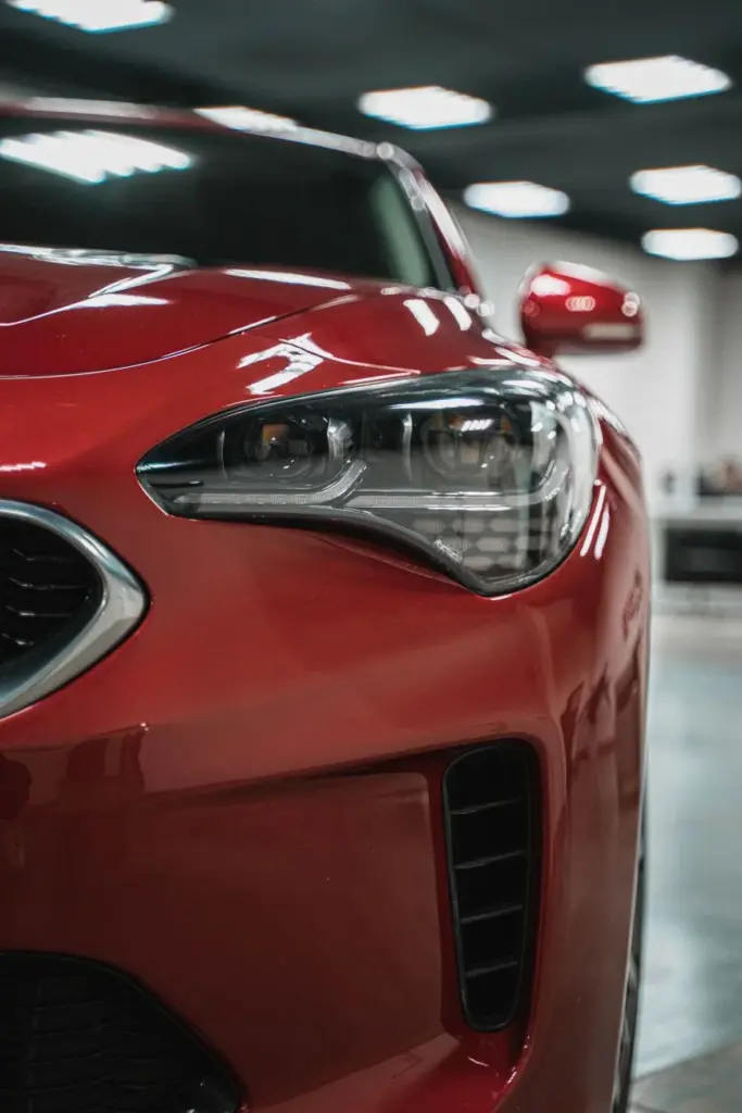Detailed view of a red sport car's headlight captured indoors with modern lighting.