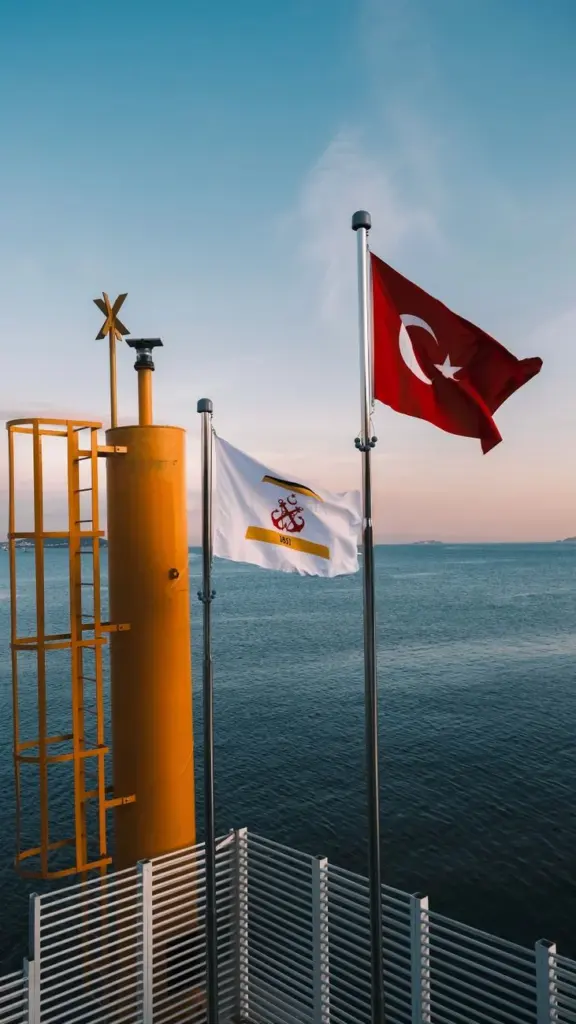 Turkish flag waving next to a metal structure by the sea during sunset.