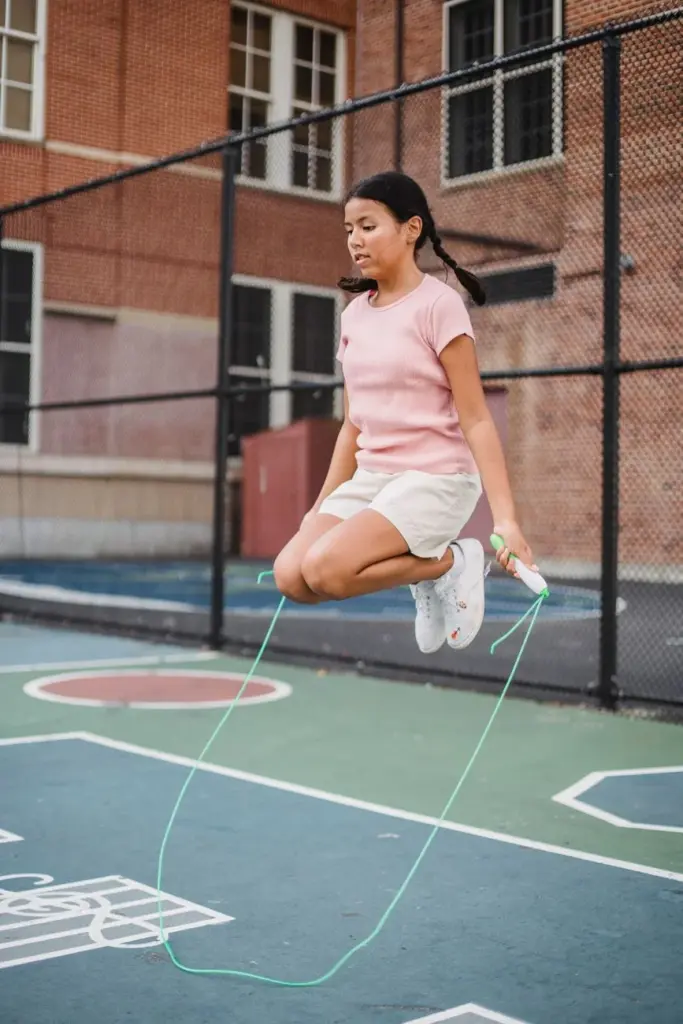 Teen girl energetically jumping rope on an outdoor basketball court, showcasing fitness and fun.