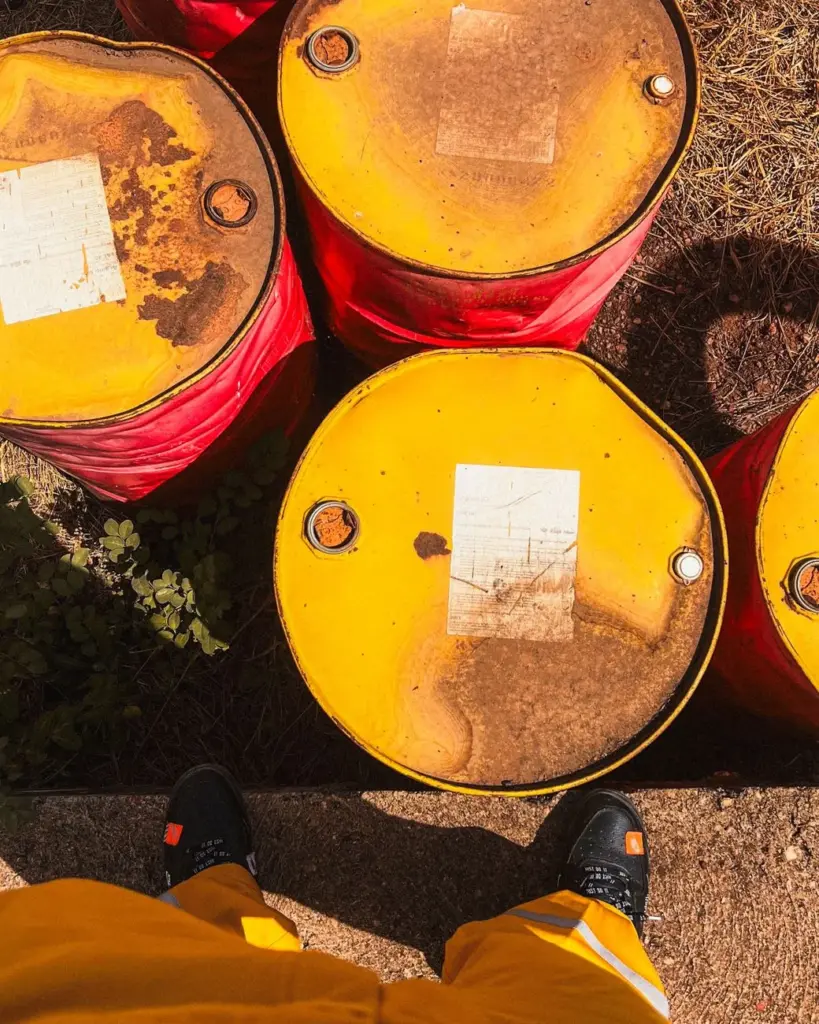 Top view of weathered yellow oil barrels on ground, person visible wearing yellow pants.