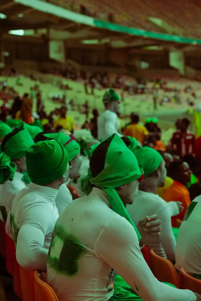 A lively festival crowd in green costumes, sitting in grandstands enjoying a performance.
