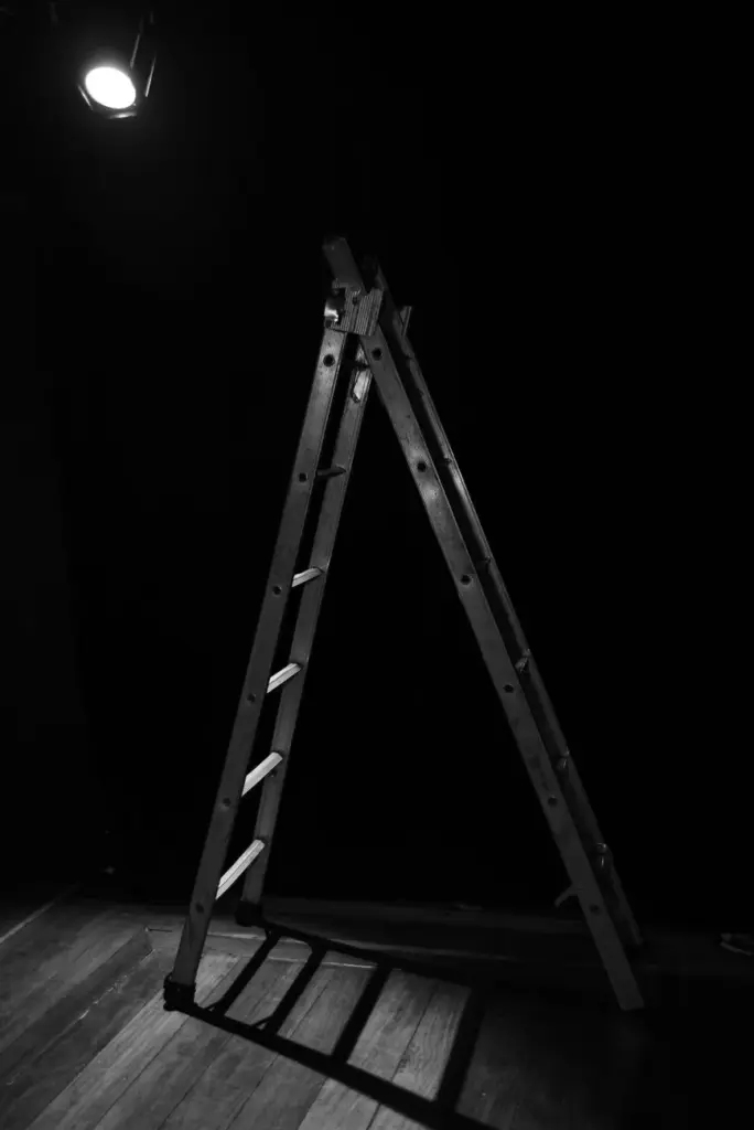 Monochrome photo of a ladder under a spotlight on a theater stage.