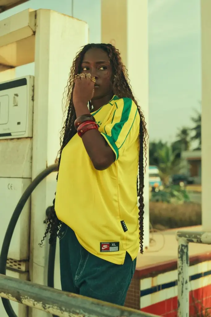 African woman in yellow jersey at a retro fuel station. Summer vibe.