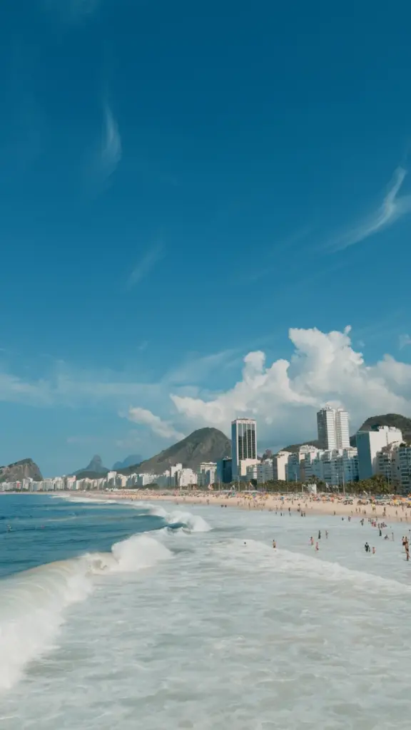 Sunny view of Copacabana Beach with waves and vibrant city skyline in Rio de Janeiro, Brazil.