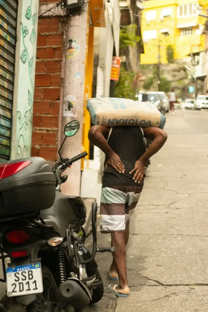 Man carries heavy cement sack in a vibrant city street, Brazil.