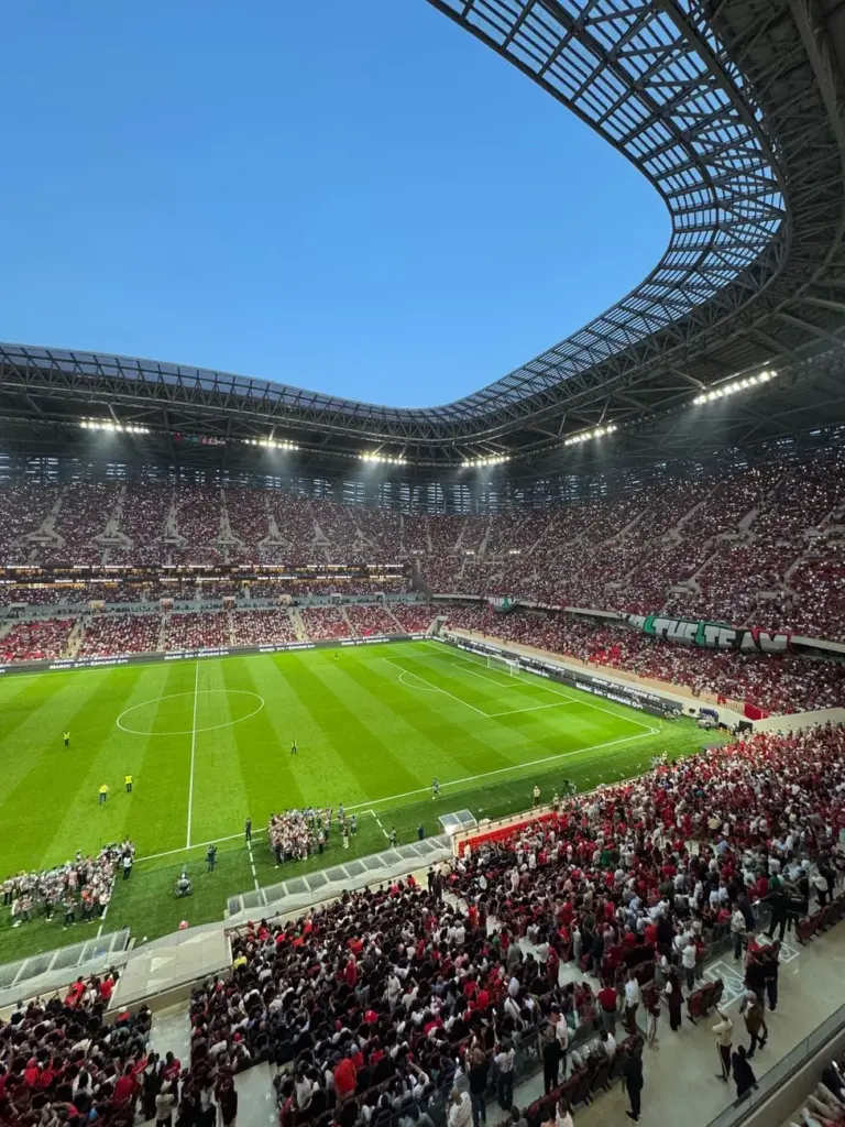 High-energy football match at a packed stadium, showcasing vibrant crowd and architecture.