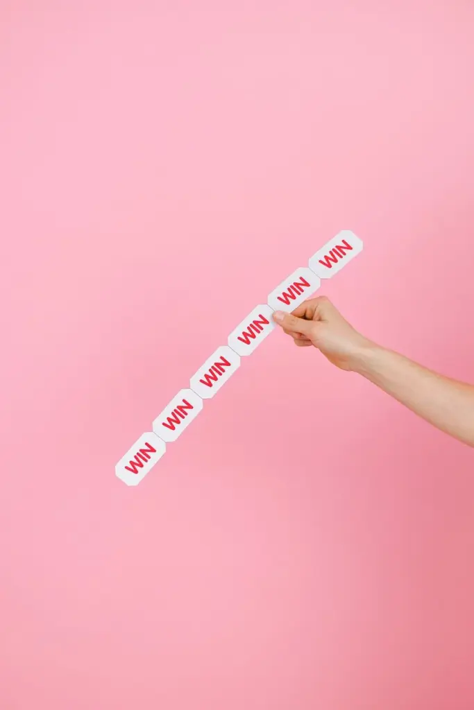 Conceptual image of a hand holding 'WIN' labels against pink background.