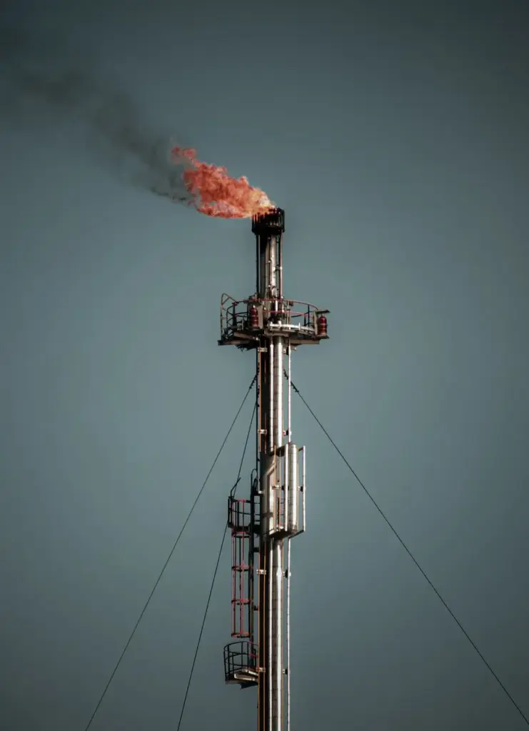 A tall industrial flare stack releasing flame and smoke, set against a clear sky, captures the essence of industrial emissions.