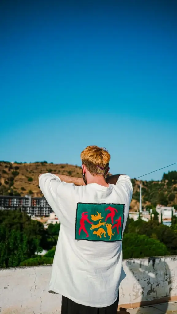 A man stands outdoors wearing a white shirt with a colorful print on the back, capturing fashion in nature.