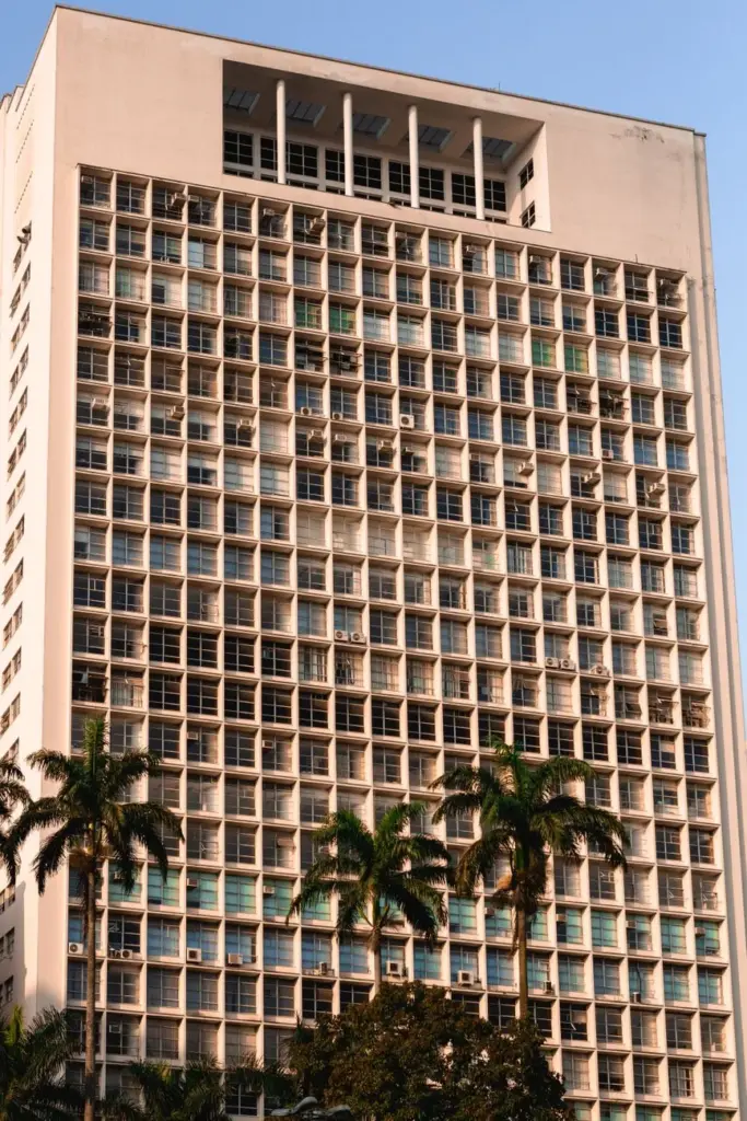 A modern high-rise building facade with palm trees under a clear blue sky.