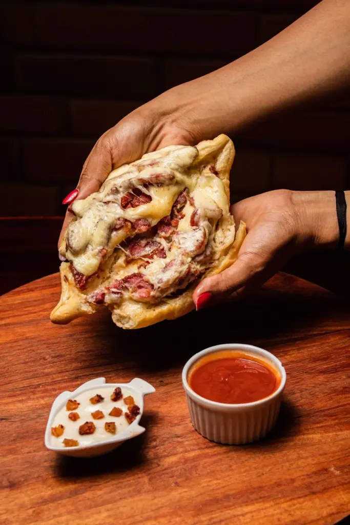 Close-up of a tasty calzone with melted cheese and meat, paired with marinara sauce and spices.