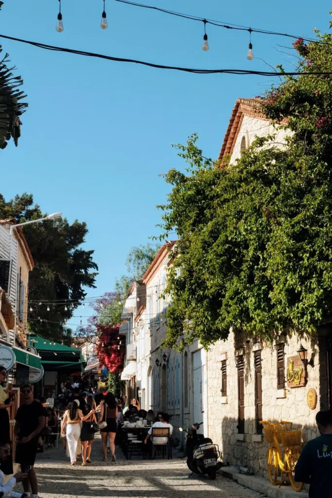 Cobblestone street with people dining and exploring in a picturesque, sunny Mediterranean town.