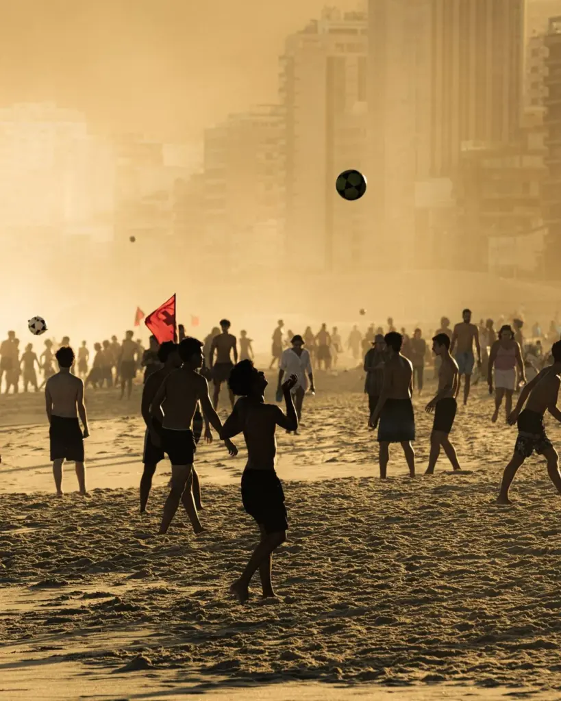 A beach soccer game at sunset with people enjoying the lively atmosphere.