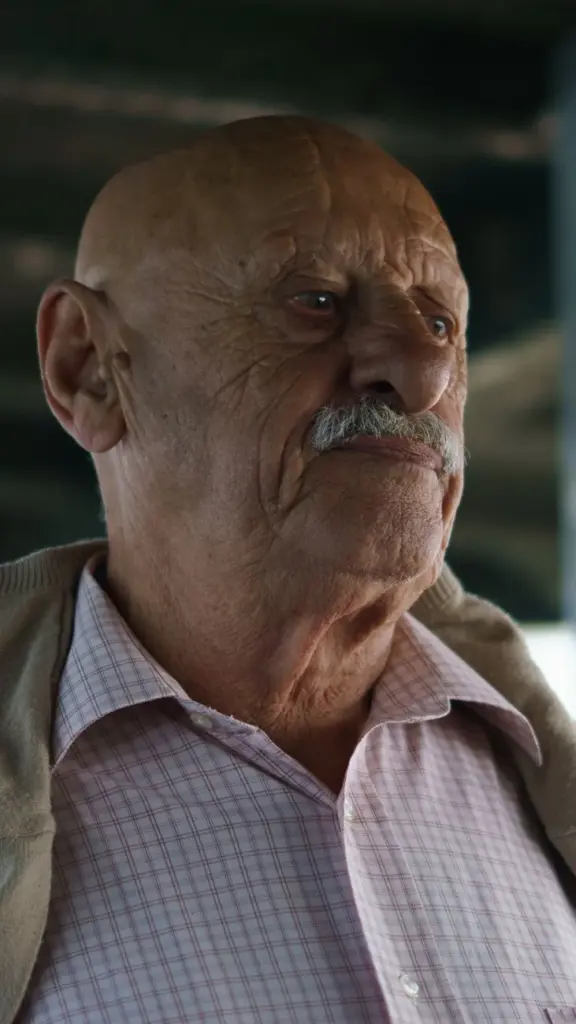 Portrait of a senior man with bald head and gray mustache in a casual jacket.